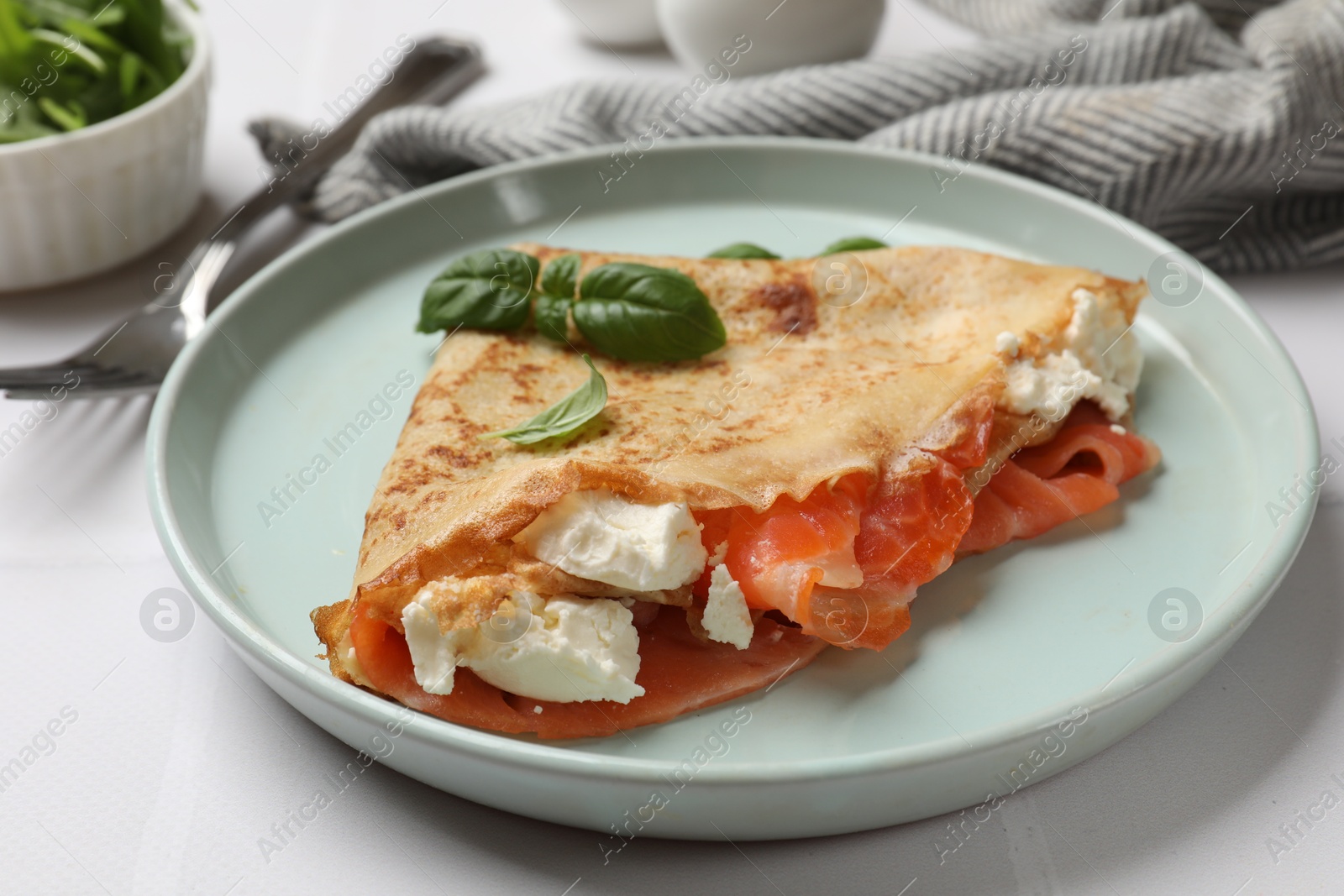 Photo of Delicious crepe with salmon, cream cheese and basil on white table, closeup