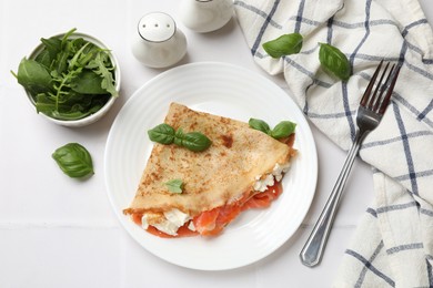 Photo of Delicious crepe with salmon, cream cheese, basil and arugula served on white tiled table, flat lay