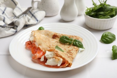 Photo of Delicious crepe with salmon, cream cheese and basil on white table, closeup