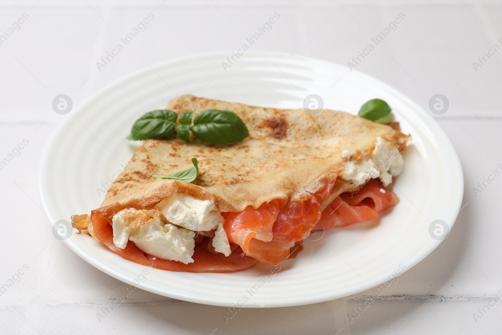 Photo of Delicious crepe with salmon, cream cheese and basil on white table, closeup