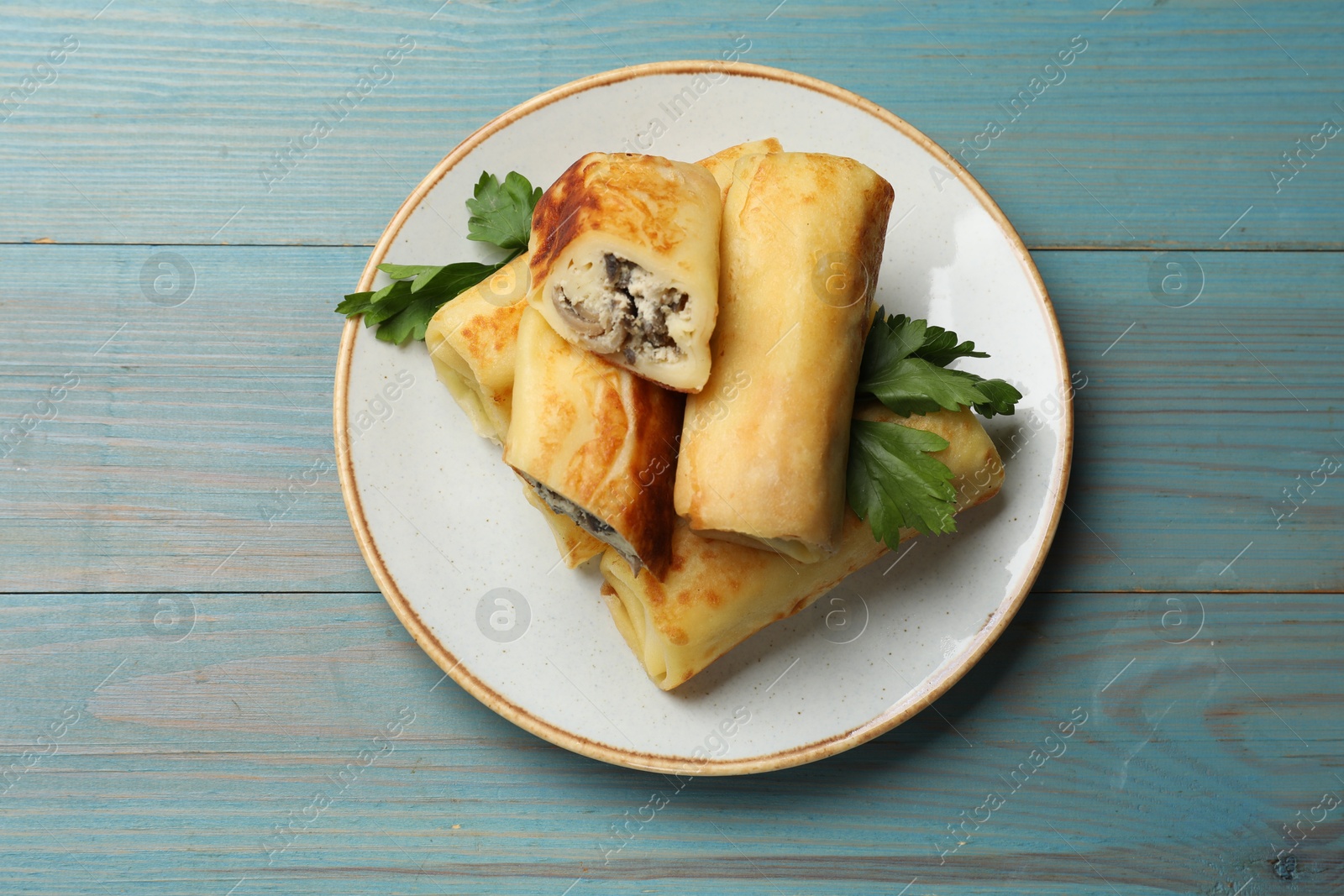 Photo of Delicious rolled crepes with mushrooms and parsley on light blue wooden table, top view