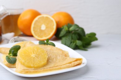 Photo of Delicious Crepes Suzette, mint and oranges on white textured table, closeup