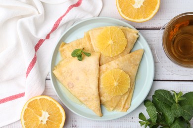 Photo of Delicious Crepes Suzette, tea and oranges on white wooden table, flat lay