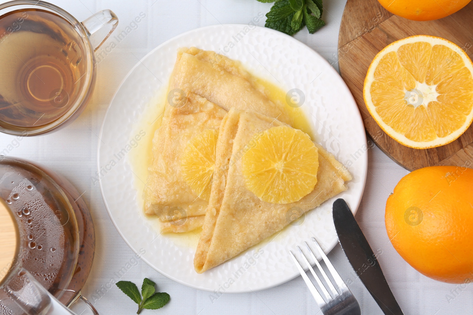 Photo of Delicious Crepes Suzette served on white tiled table, flat lay