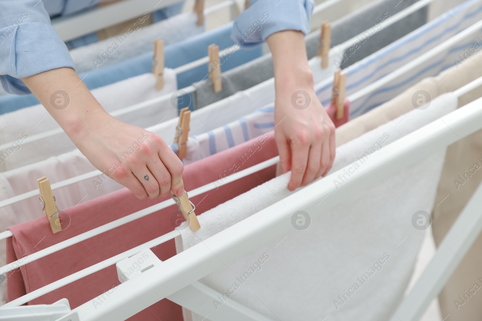 Photo of Woman hanging fresh clean laundry on drying rack at home, closeup