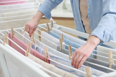 Photo of Woman hanging fresh clean laundry on drying rack at home, closeup