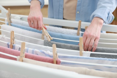 Photo of Woman hanging fresh clean laundry on drying rack at home, closeup