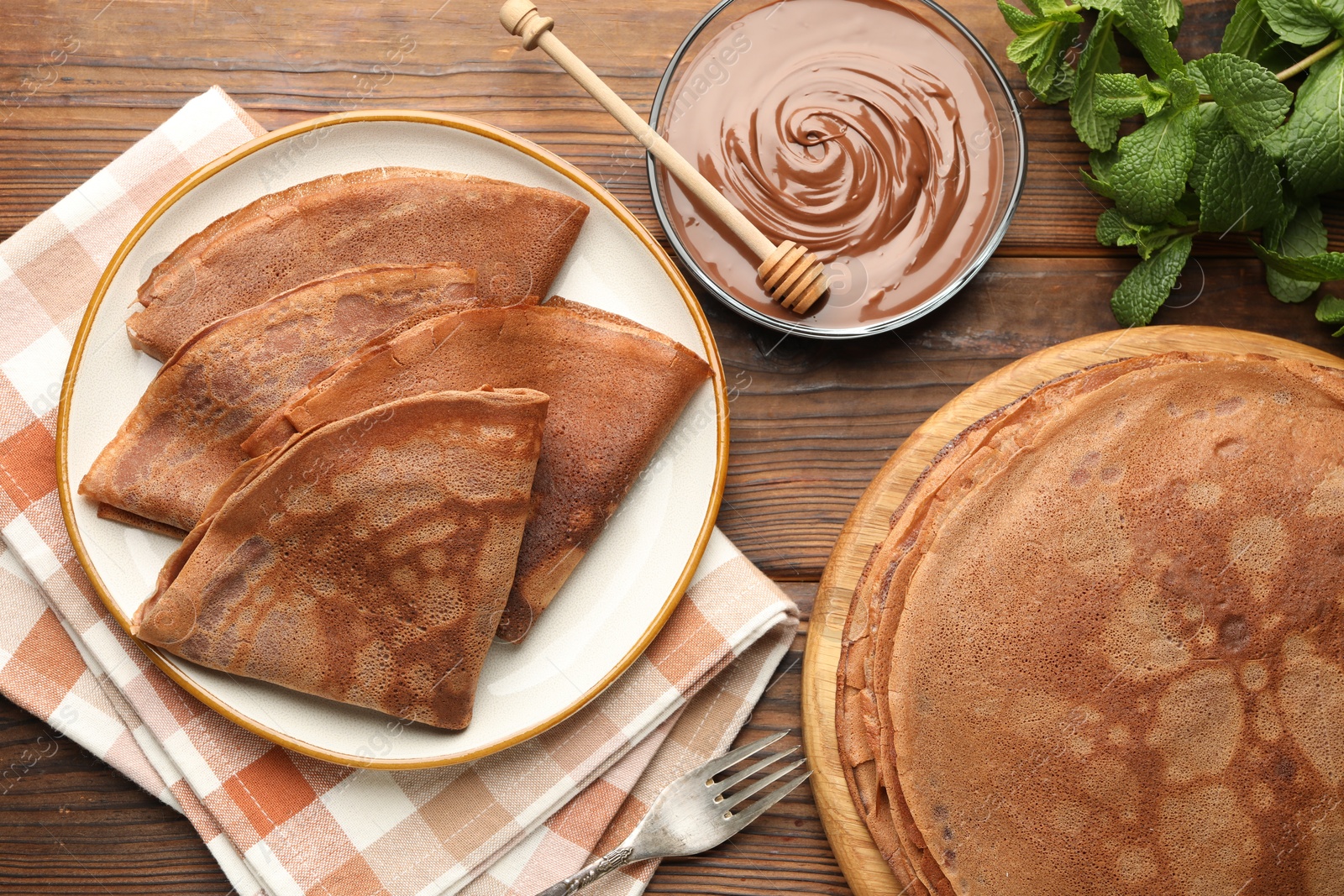 Photo of Delicious chocolate crepes, sweet sauce and mint on wooden table, flat lay