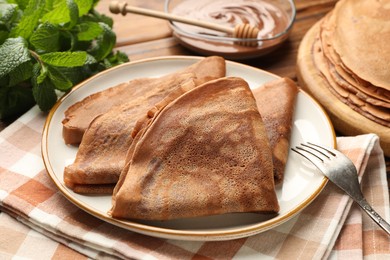 Photo of Delicious chocolate crepes, sweet sauce and mint on wooden table, closeup