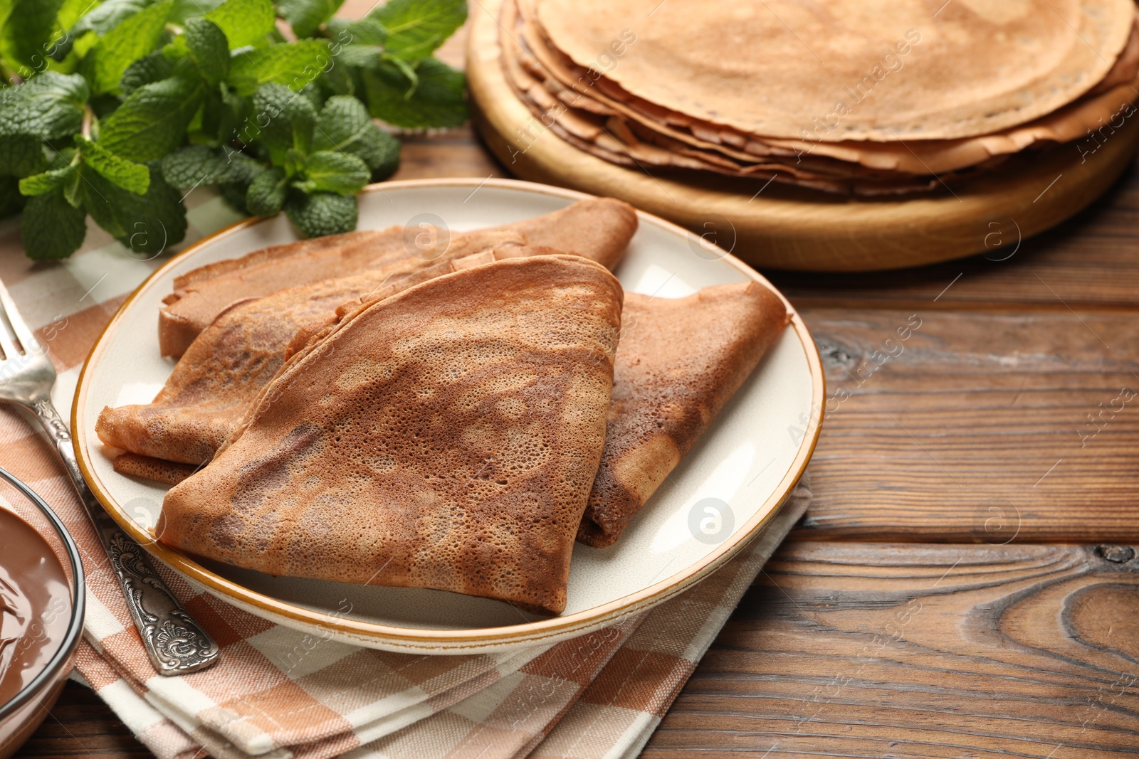 Photo of Delicious chocolate crepes and mint on wooden table, closeup