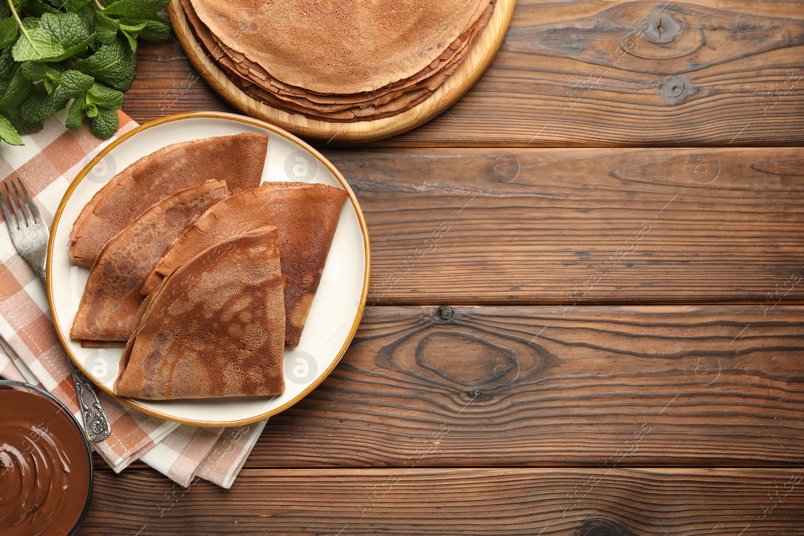 Photo of Delicious chocolate crepes, sweet sauce and mint on wooden table, flat lay. Space for text