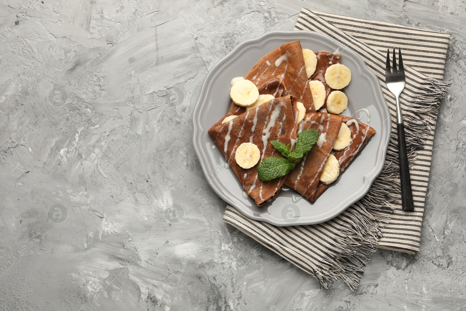 Photo of Delicious chocolate crepes with banana, condensed milk and mint served on grey table, top view. Space for text