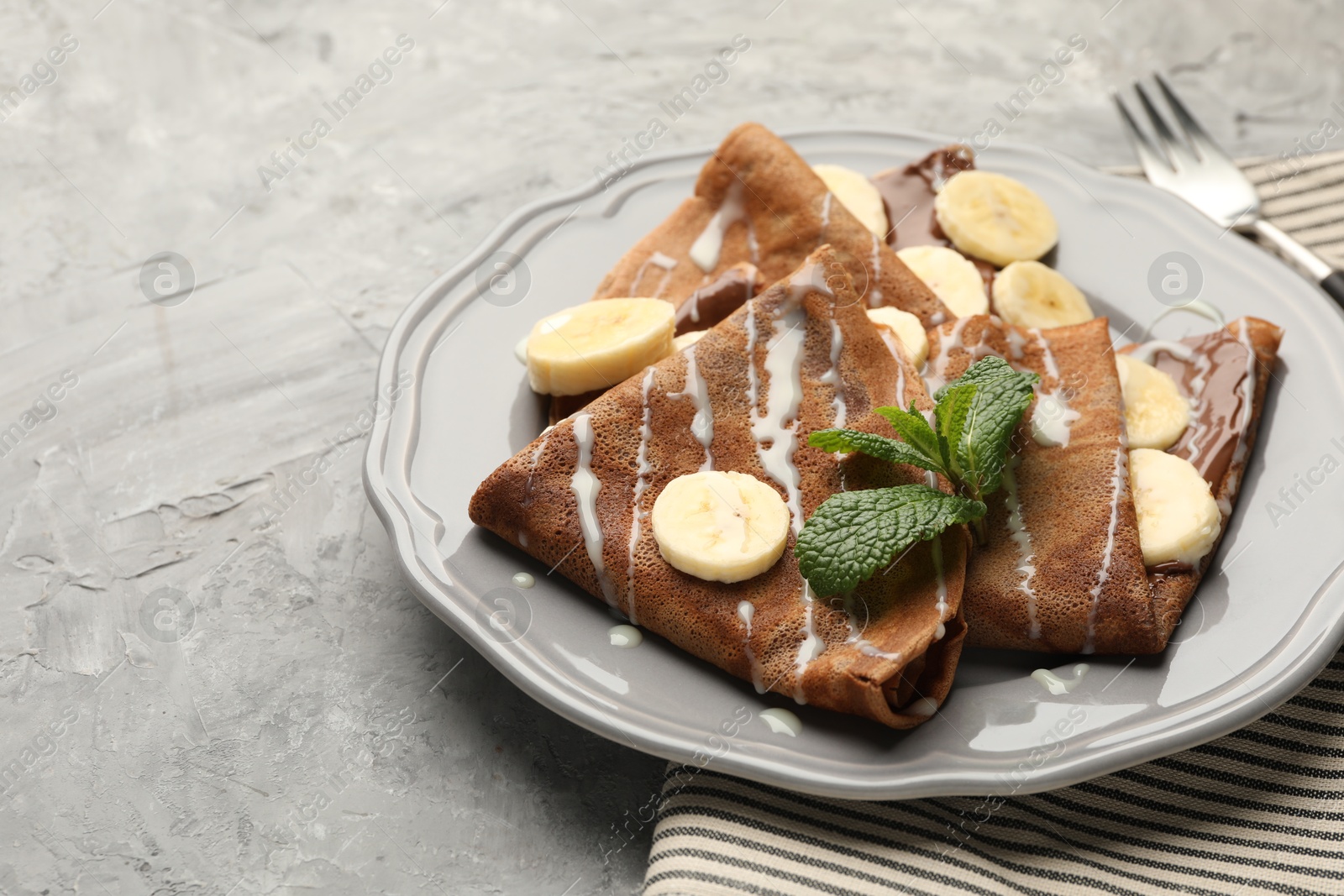 Photo of Delicious chocolate crepes with banana, condensed milk and mint served on grey table, closeup