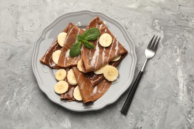 Photo of Delicious chocolate crepes with banana, condensed milk and mint served on grey table, top view