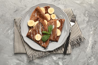 Photo of Delicious chocolate crepes with banana, condensed milk and mint served on grey table, top view