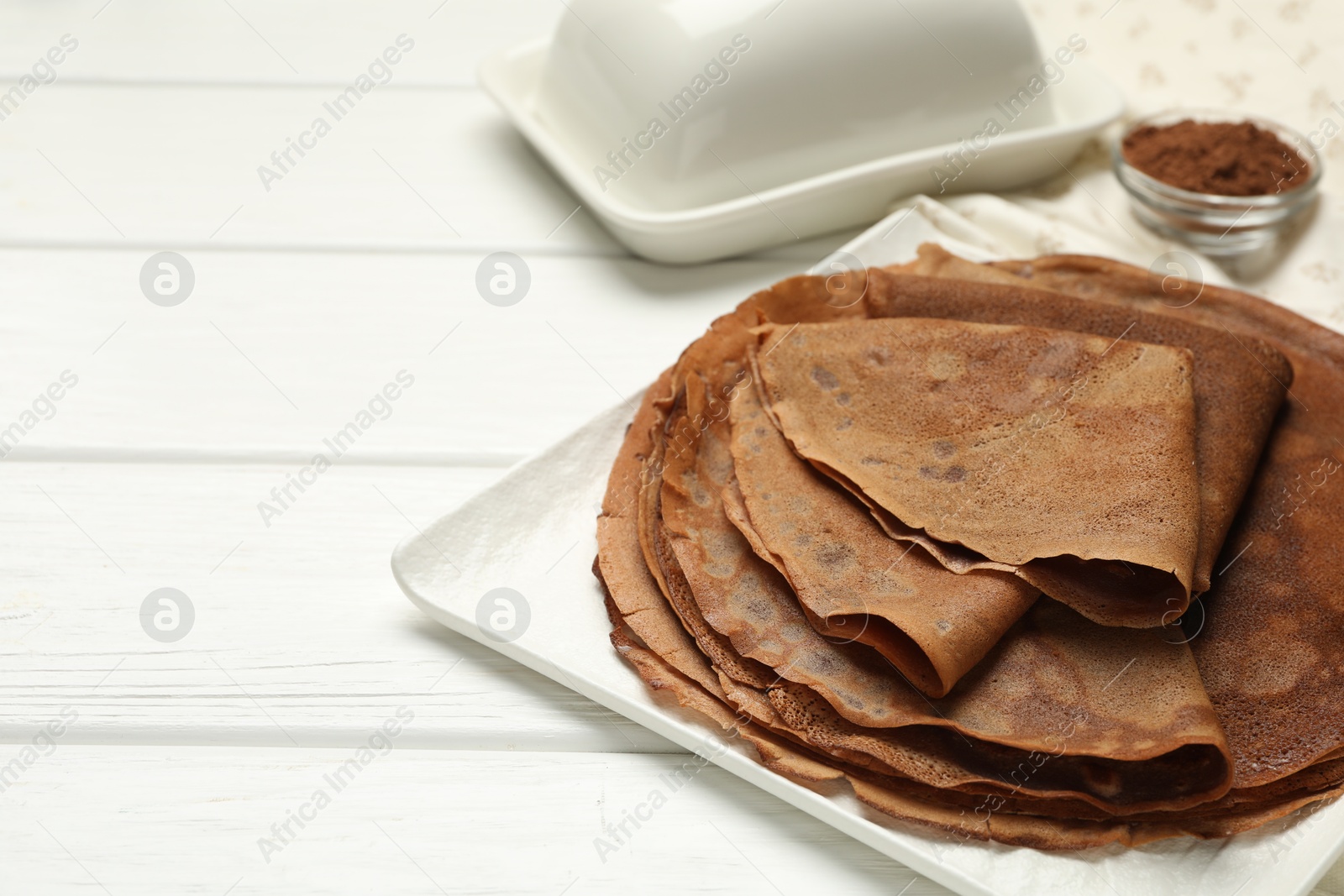 Photo of Delicious chocolate crepes and cocoa powder on white wooden table, closeup. Space for text