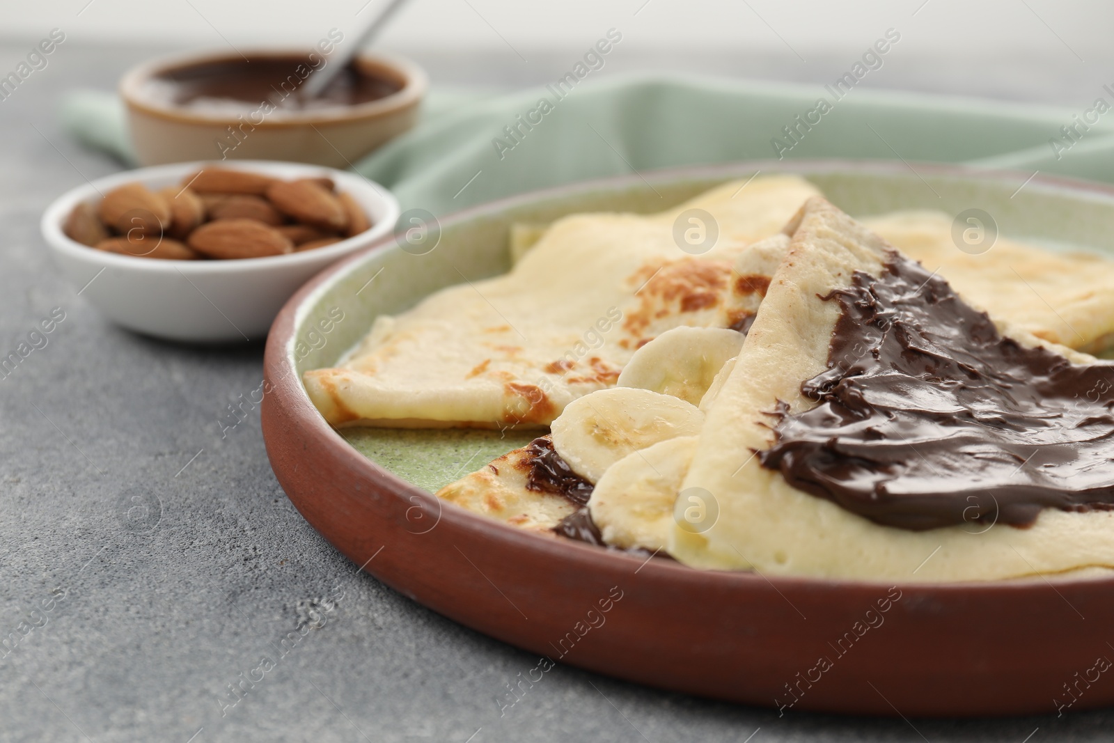 Photo of Delicious crepes with chocolate sauce and banana on grey table, closeup