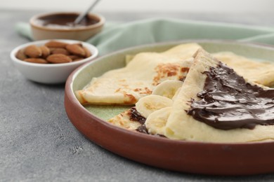 Photo of Delicious crepes with chocolate sauce and banana on grey table, closeup