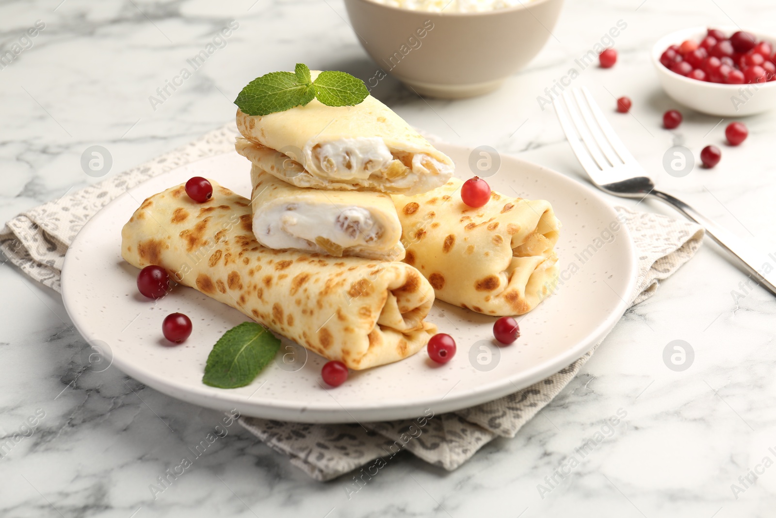 Photo of Delicious rolled crepes with cottage cheese, raisins, cranberries and mint on white marble table, closeup