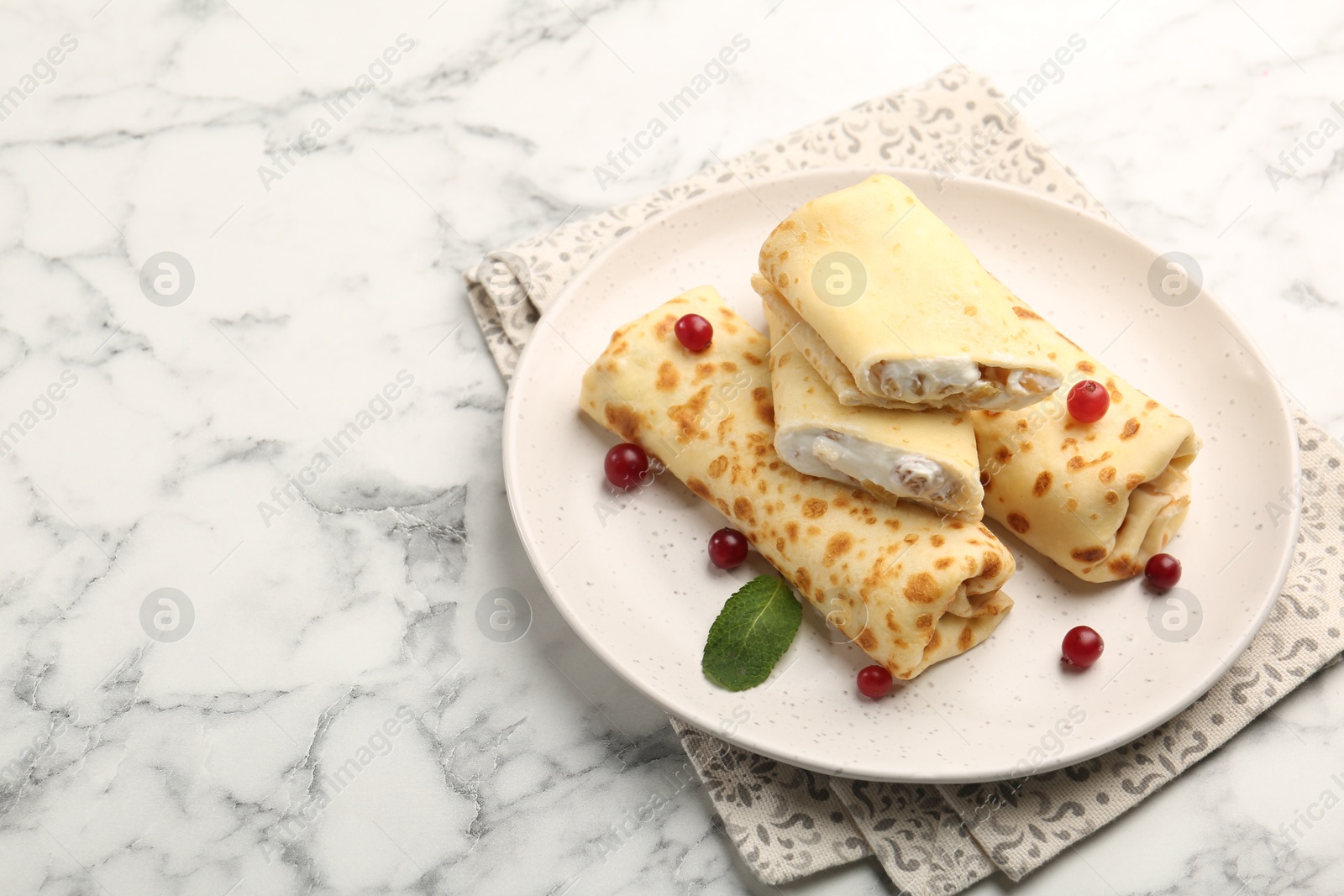 Photo of Delicious rolled crepes with cottage cheese, raisins, cranberries and mint on white marble table, space for text