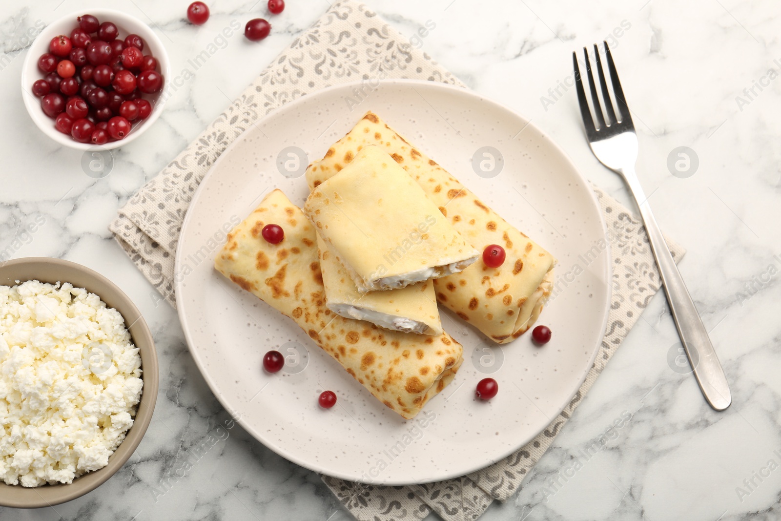 Photo of Delicious rolled crepes with cottage cheese, raisins and cranberries on white marble table, flat lay