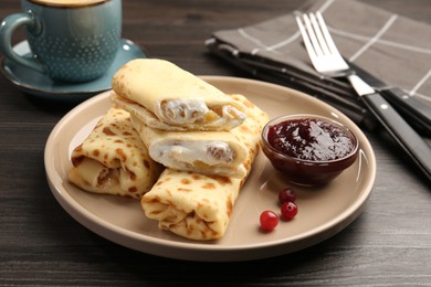 Photo of Delicious rolled crepes with cottage cheese, raisins, jam and cranberries on wooden table, closeup