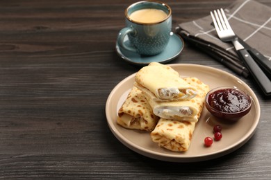 Photo of Delicious rolled crepes with cottage cheese, raisins, jam, cranberries and coffee on wooden table, space for text