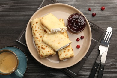 Photo of Delicious rolled crepes with cottage cheese, raisins, jam, cranberries and coffee on wooden table, flat lay