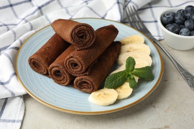 Photo of Delicious chocolate crepes with banana and blueberries served on light table, closeup