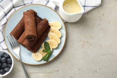 Photo of Delicious chocolate crepes with banana and blueberries served on light table, flat lay