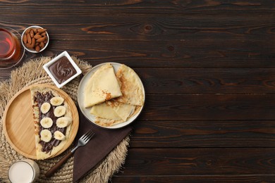 Delicious crepes with chocolate paste and banana served on wooden table, flat lay. Space for text