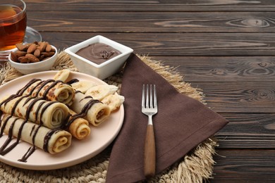 Photo of Delicious crepes with chocolate sauce served on wooden table. Space for text