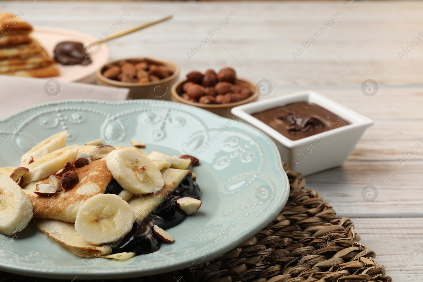 Photo of Delicious crepes with banana, chocolate sauce and nuts on wooden table, closeup