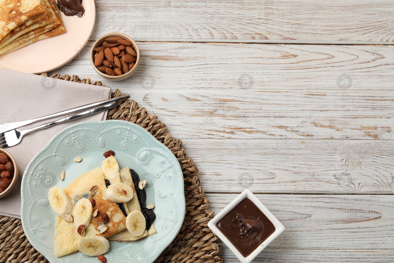 Photo of Delicious crepes with banana, chocolate sauce and nuts on wooden table, flat lay. Space for text