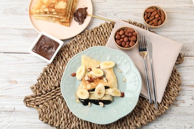 Delicious crepes with banana, chocolate sauce and nuts on wooden table, flat lay