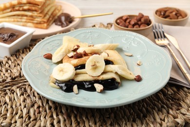 Photo of Delicious crepes with banana, chocolate sauce and nuts on table, closeup