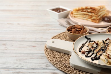 Photo of Delicious crepes with banana, chocolate sauce and nuts on wooden table, closeup. Space for text