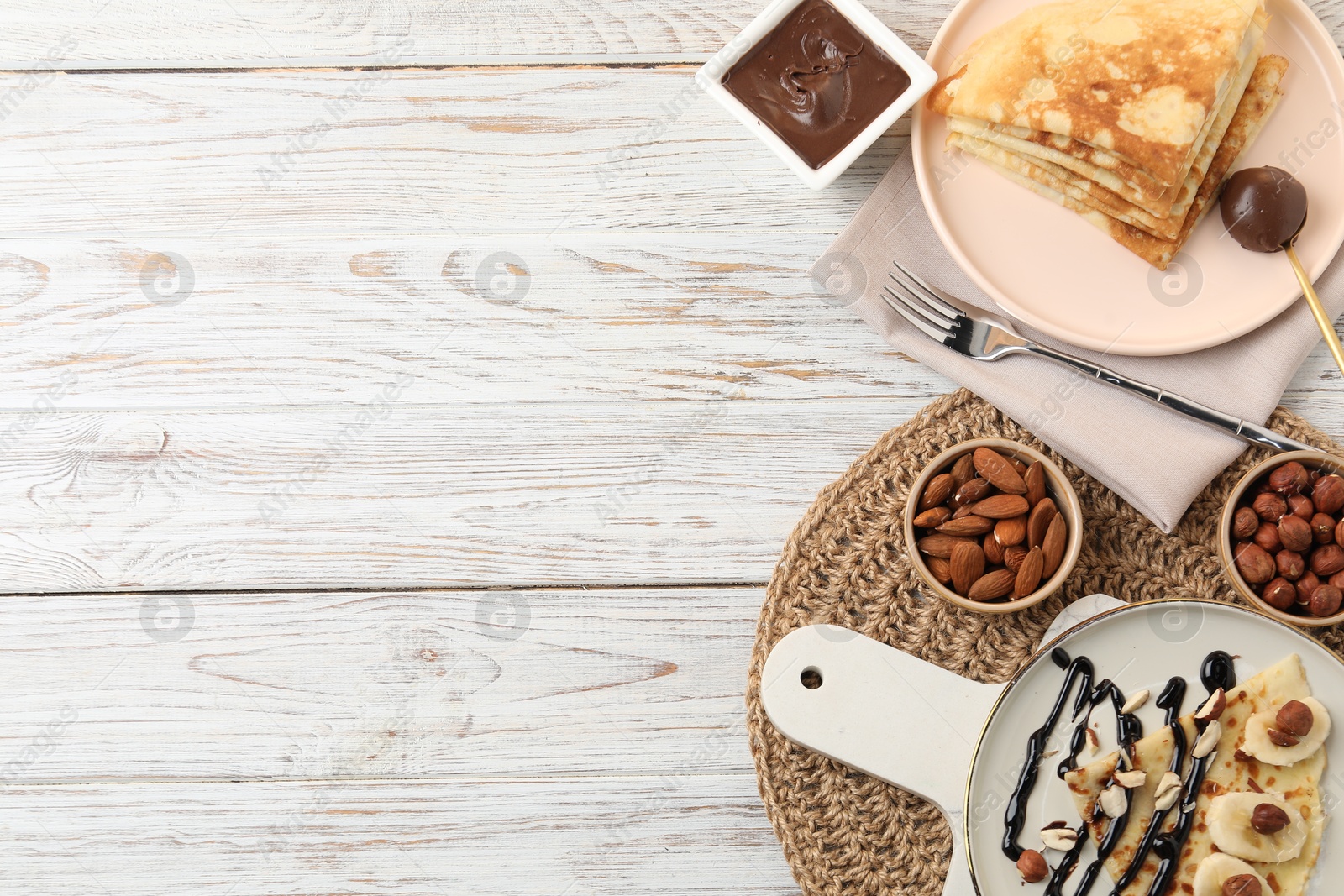 Photo of Delicious crepes served with chocolate sauce and nuts on wooden table, flat lay. Space for text