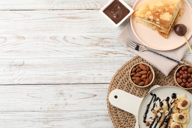 Photo of Delicious crepes served with chocolate sauce and nuts on wooden table, flat lay. Space for text