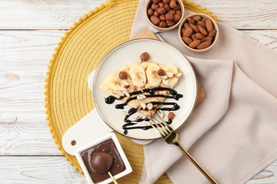 Photo of Delicious crepe with banana, chocolate sauce and nuts on wooden table, flat lay