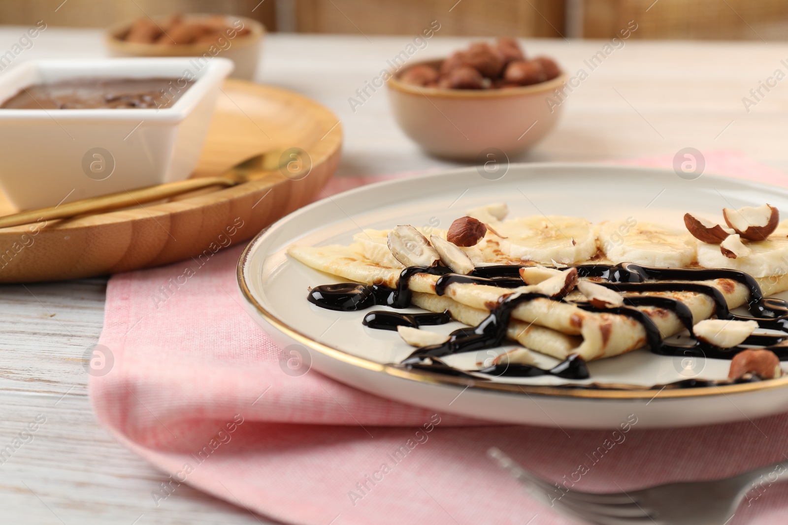 Photo of Delicious crepe with banana, nuts and chocolate sauce on wooden table, closeup