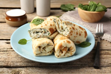 Photo of Tasty rolled crepes with cottage cheese and spinach served on wooden table, closeup