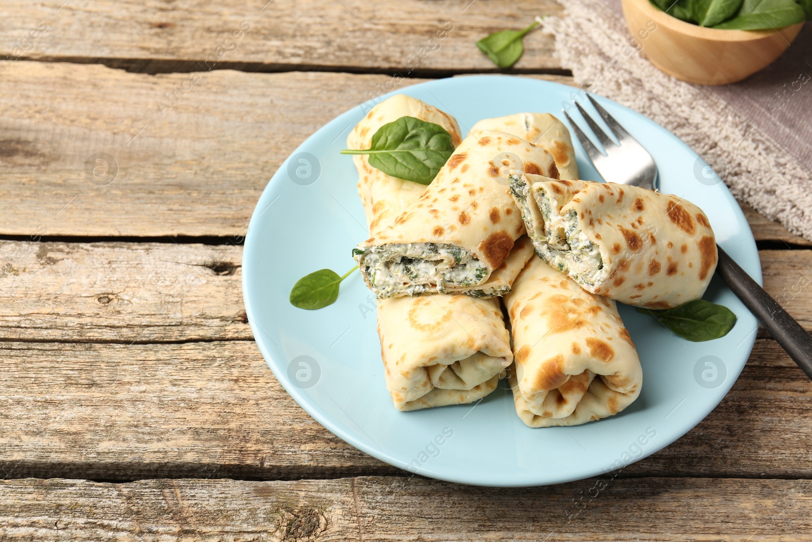 Photo of Tasty rolled crepes with cottage cheese and spinach served on wooden table, closeup. Space for text