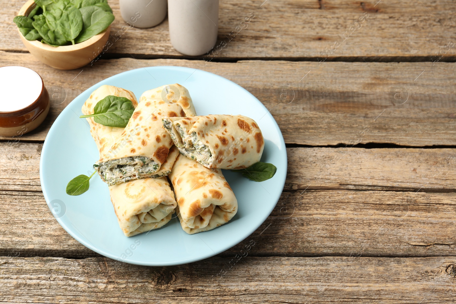 Photo of Tasty rolled crepes with cottage cheese and spinach served on wooden table, closeup. Space for text