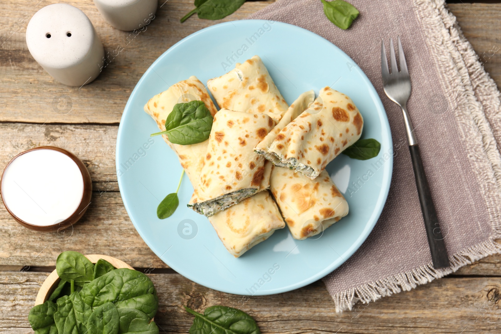 Photo of Tasty rolled crepes with cottage cheese and spinach served on wooden table, flat lay