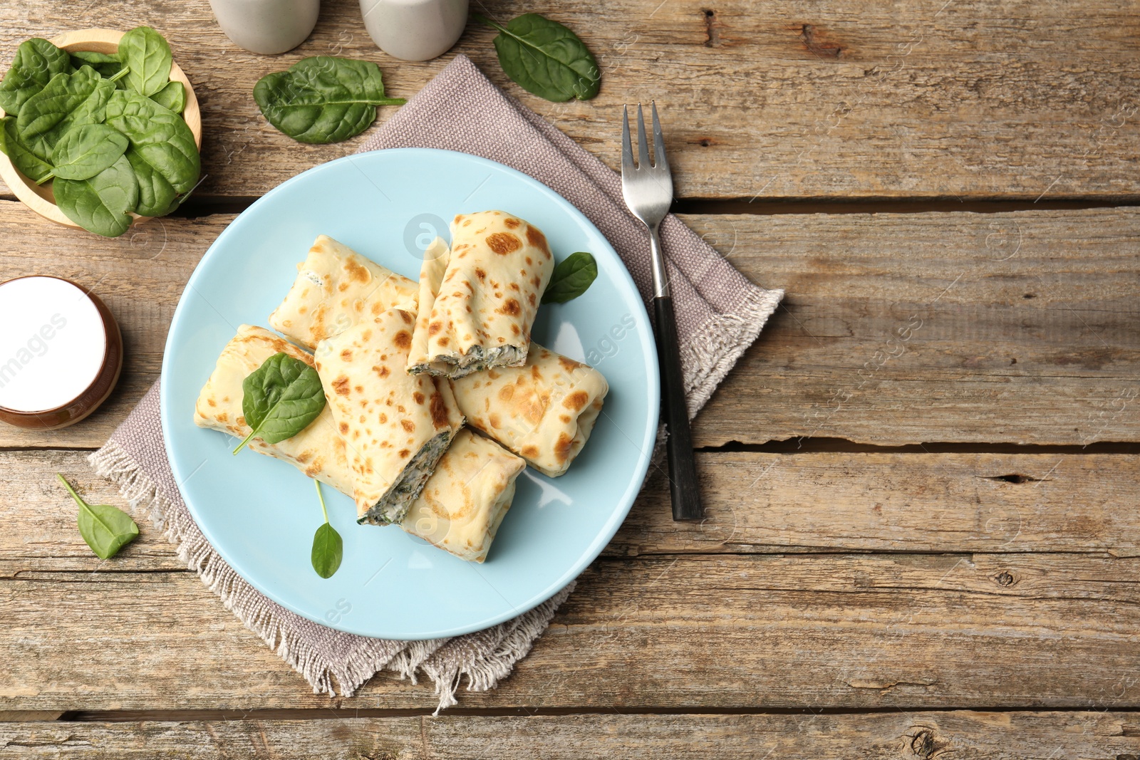 Photo of Tasty rolled crepes with cottage cheese and spinach served on wooden table, flat lay. Space for text