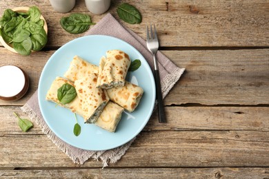 Photo of Tasty rolled crepes with cottage cheese and spinach served on wooden table, flat lay. Space for text