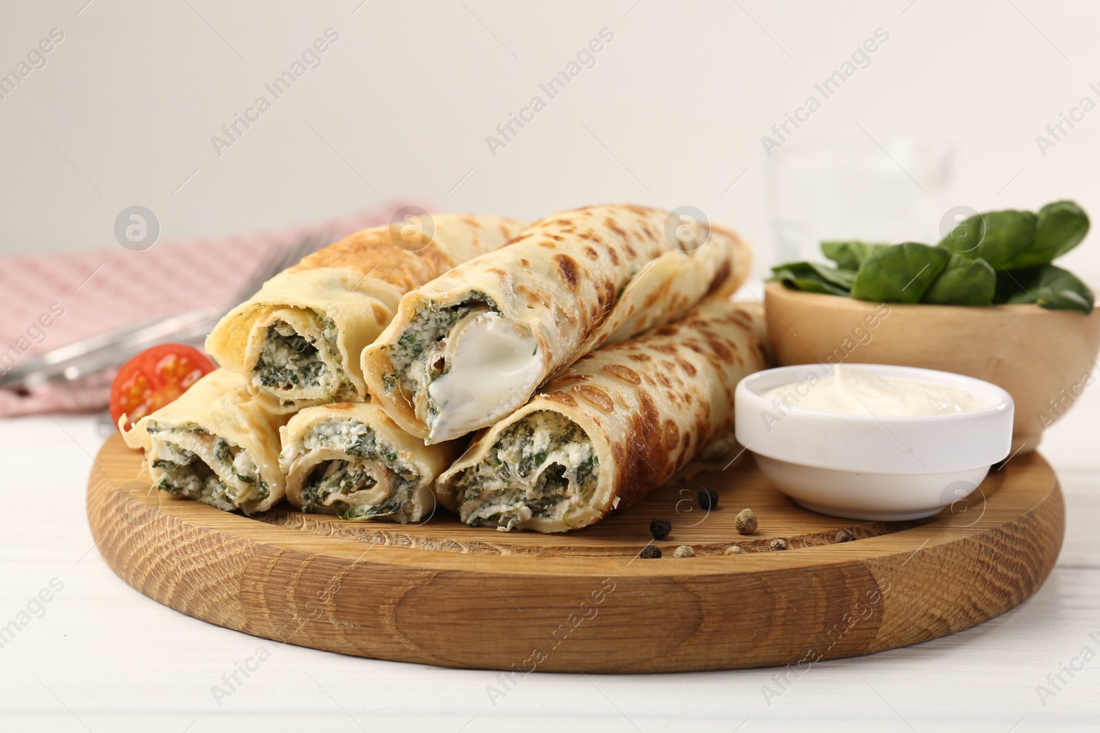 Photo of Tasty rolled crepes with cottage cheese and spinach served on white wooden table, closeup