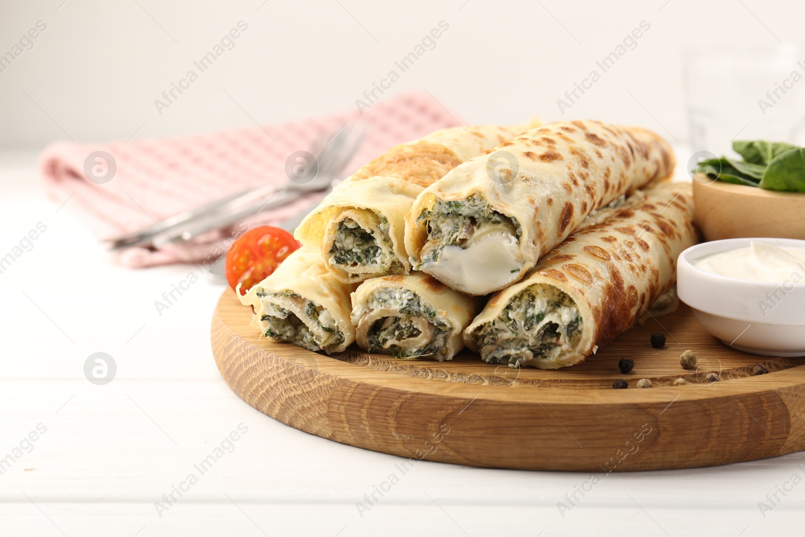 Photo of Tasty rolled crepes with cottage cheese and spinach served on white wooden table, closeup