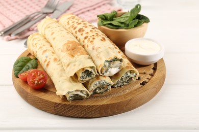 Photo of Tasty rolled crepes with cottage cheese and spinach served on white wooden table, closeup